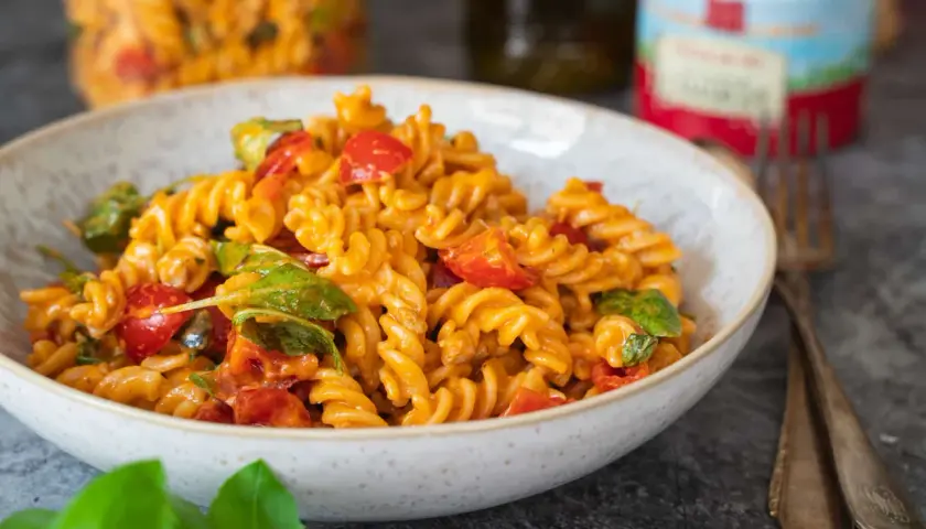 Ein köstlicher Nudelsalat mit Pesto, Kirschtomaten und frischem Basilikum in einer Schüssel.