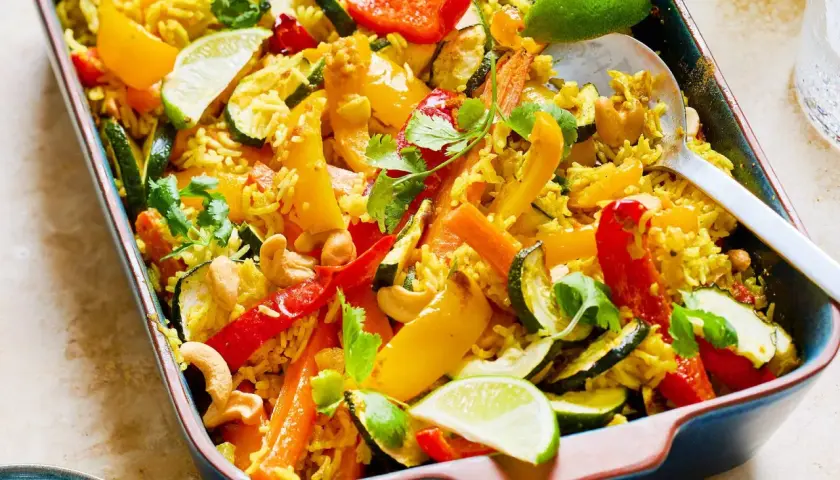 Buntes Gericht mit Reis, Paprika, Zucchini, Karotten und Cashewkernen, garniert mit Koriander und Limettenspalten. Ein köstliches Gericht mit Reis.