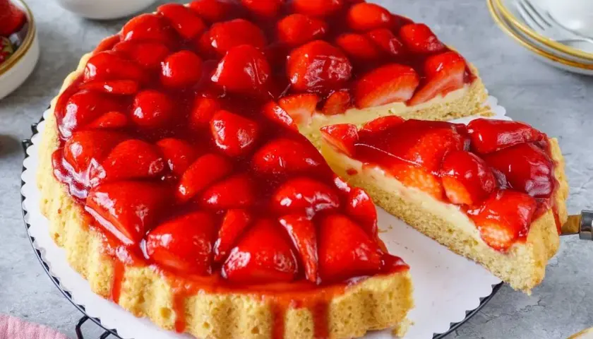 Ein saftiger Kuchen mit Erdbeeren, bedeckt mit glänzendem Tortenguss. Ein Stück wurde bereits entnommen, um die cremige Füllung zu enthüllen.