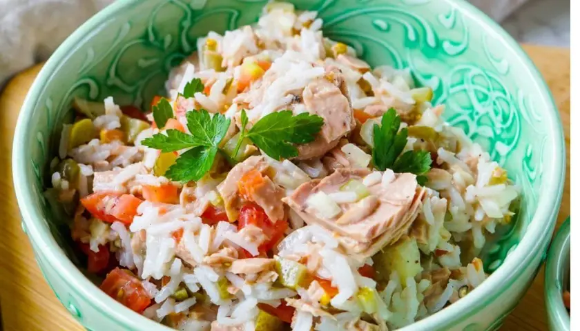 Reissalat mit Thunfisch, Tomaten und Gurken, garniert mit Petersilie, in einer grünen Schüssel.