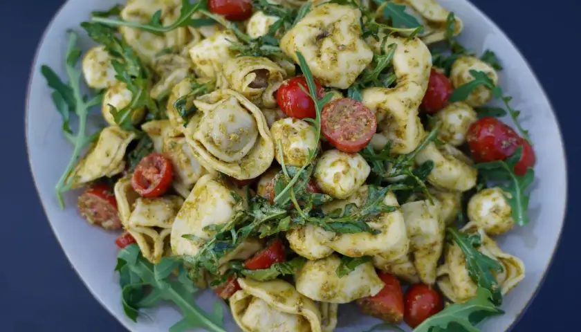 Mediterraner Salat mit Tortellini, Mozzarella-Bällchen, Kirschtomaten und Rucola, verfeinert mit Pesto.