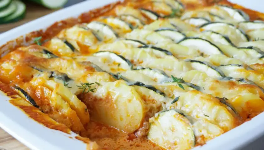 Herzhafter zucchini hackfleisch auflauf mit Kartoffeln und Käse überbacken, garniert mit frischen Kräutern.