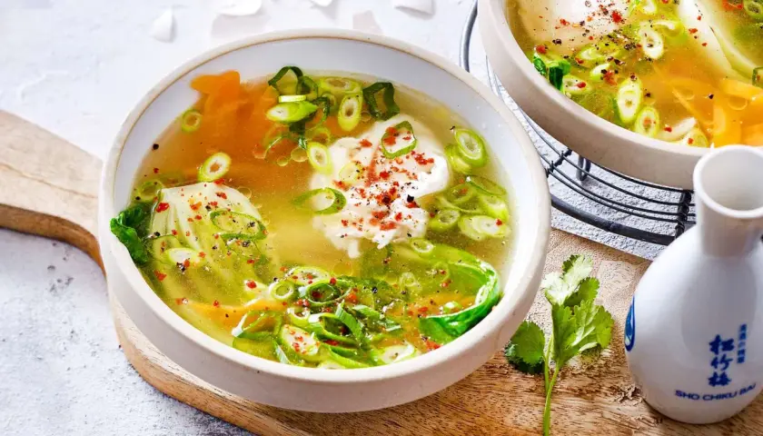 Zwei Schalen dampfender low carb suppe mit pochiertem Ei, Frühlingszwiebeln und Pak Choi, garniert mit Chiliflocken.