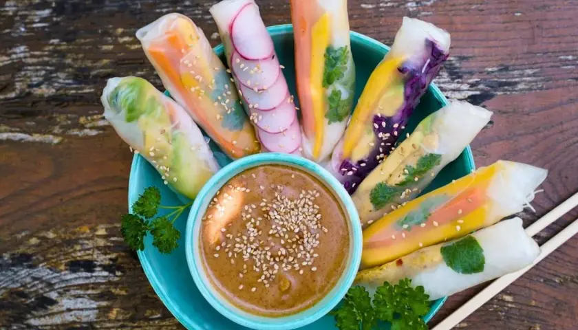 Frische Sommerrollen mit bunten Gemüsesorten, garniert mit Sesam, serviert mit Erdnussdip. Perfekt für ein leichtes Sommerrollen Rezept.