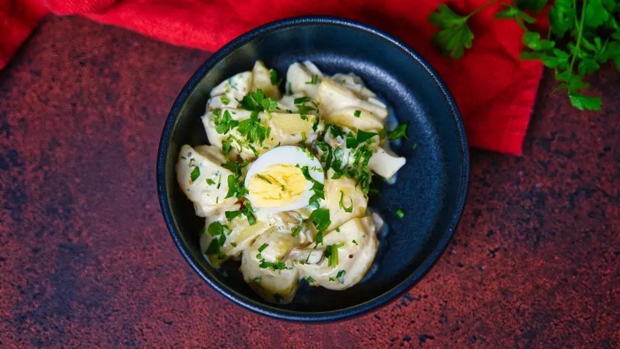 Ein cremiger Kartoffelsalat mit Mayo, garniert mit Petersilie und einem halben Ei. Perfekt für ein Picknick!