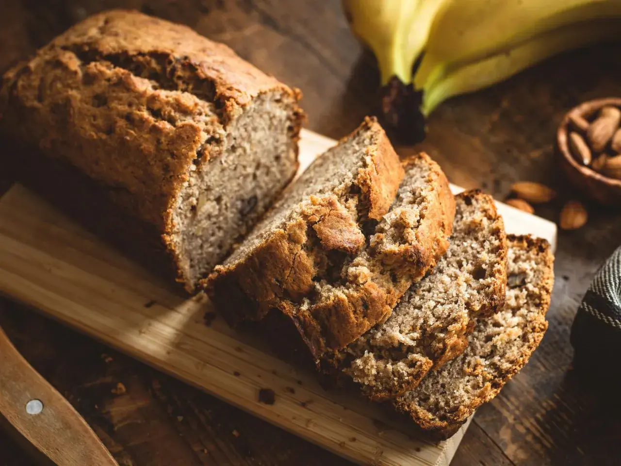 Ein saftiges Bananenbrot, perfekt für ein Bananenbrot Rezept ohne Zucker. Daneben liegen Mandeln und reife Bananen.