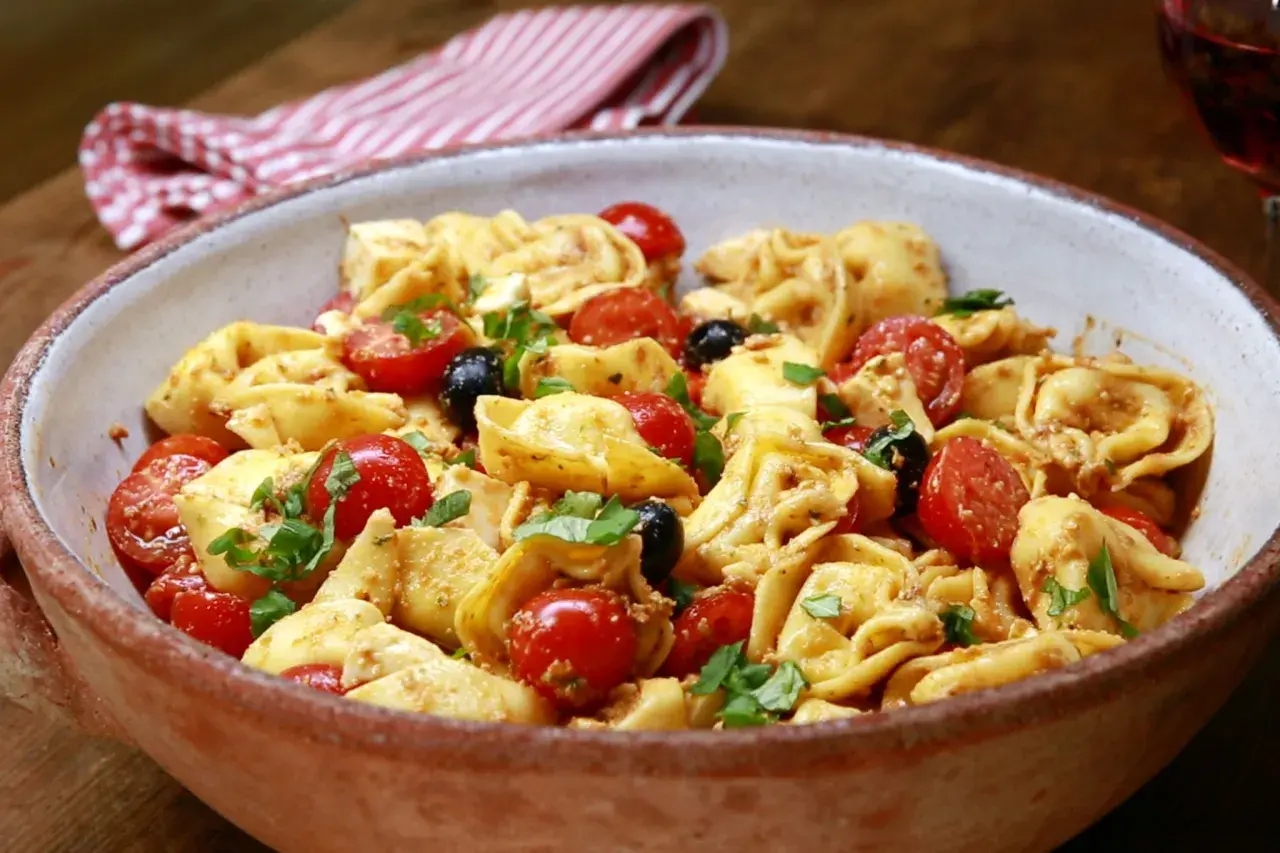 Herzhafter Tortellini Salat mit Kirschtomaten, schwarzen Oliven und frischem Basilikum in einer rustikalen Schüssel.