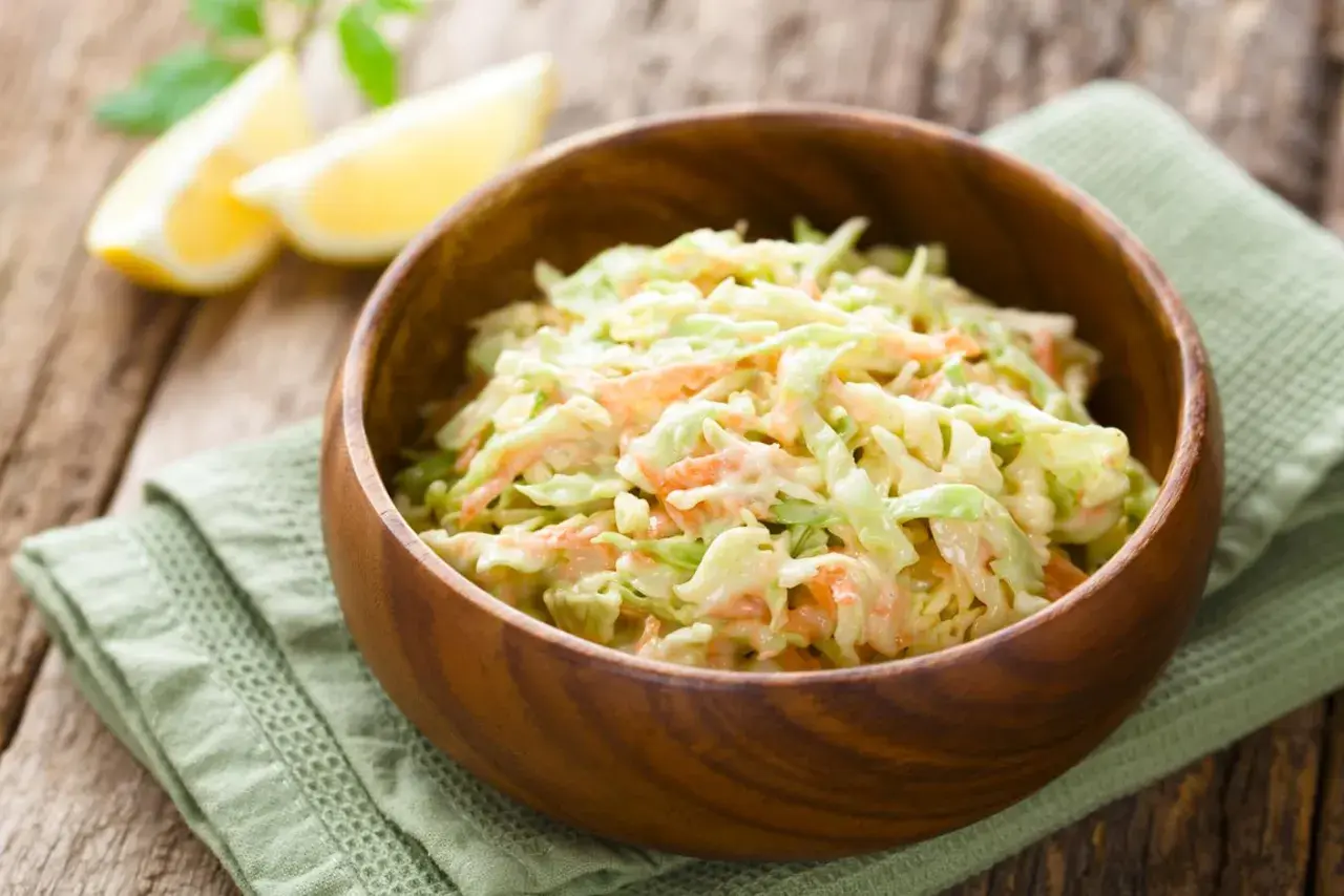 Cremiger Krautsalat mit Karotten, perfekt für jedes BBQ. Ein einfaches coleslaw rezept, das immer gelingt. Serviert in einer Holzschale mit Zitronenspalten.