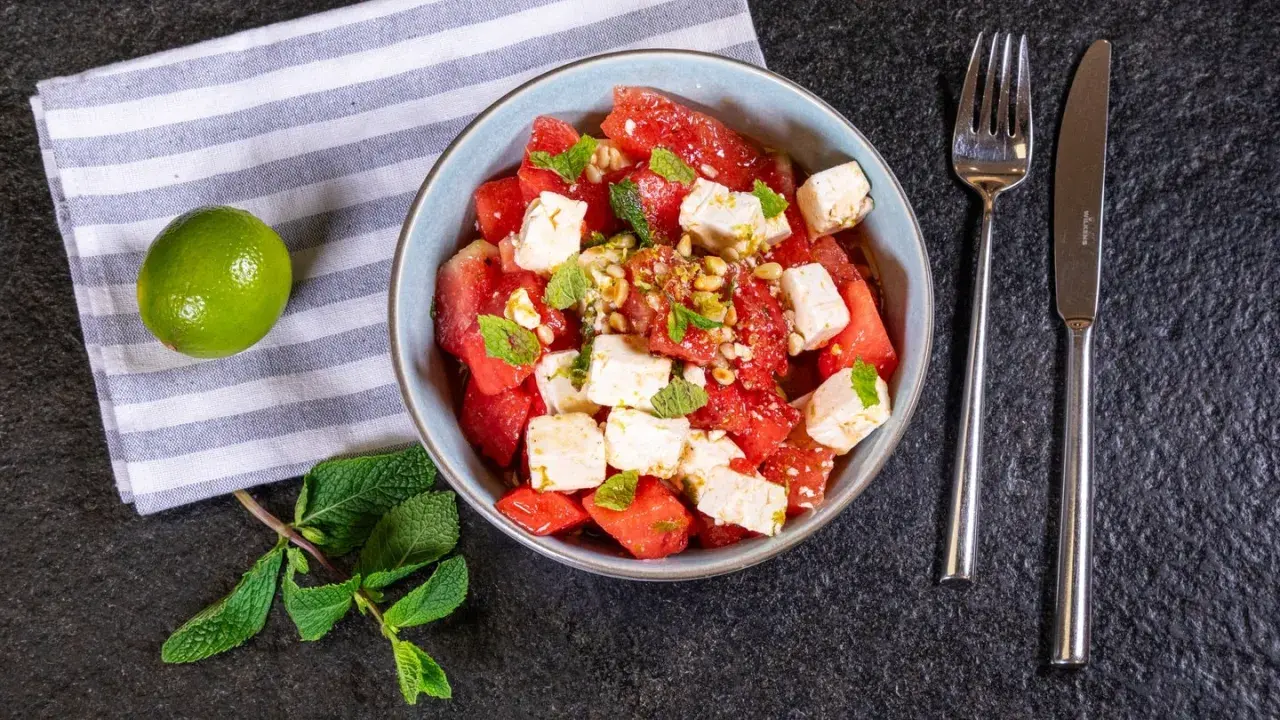 Erfrischender Wassermelonen Feta Salat mit Minze und Pinienkernen, garniert mit Limettenabrieb. Perfekt für heiße Tage!