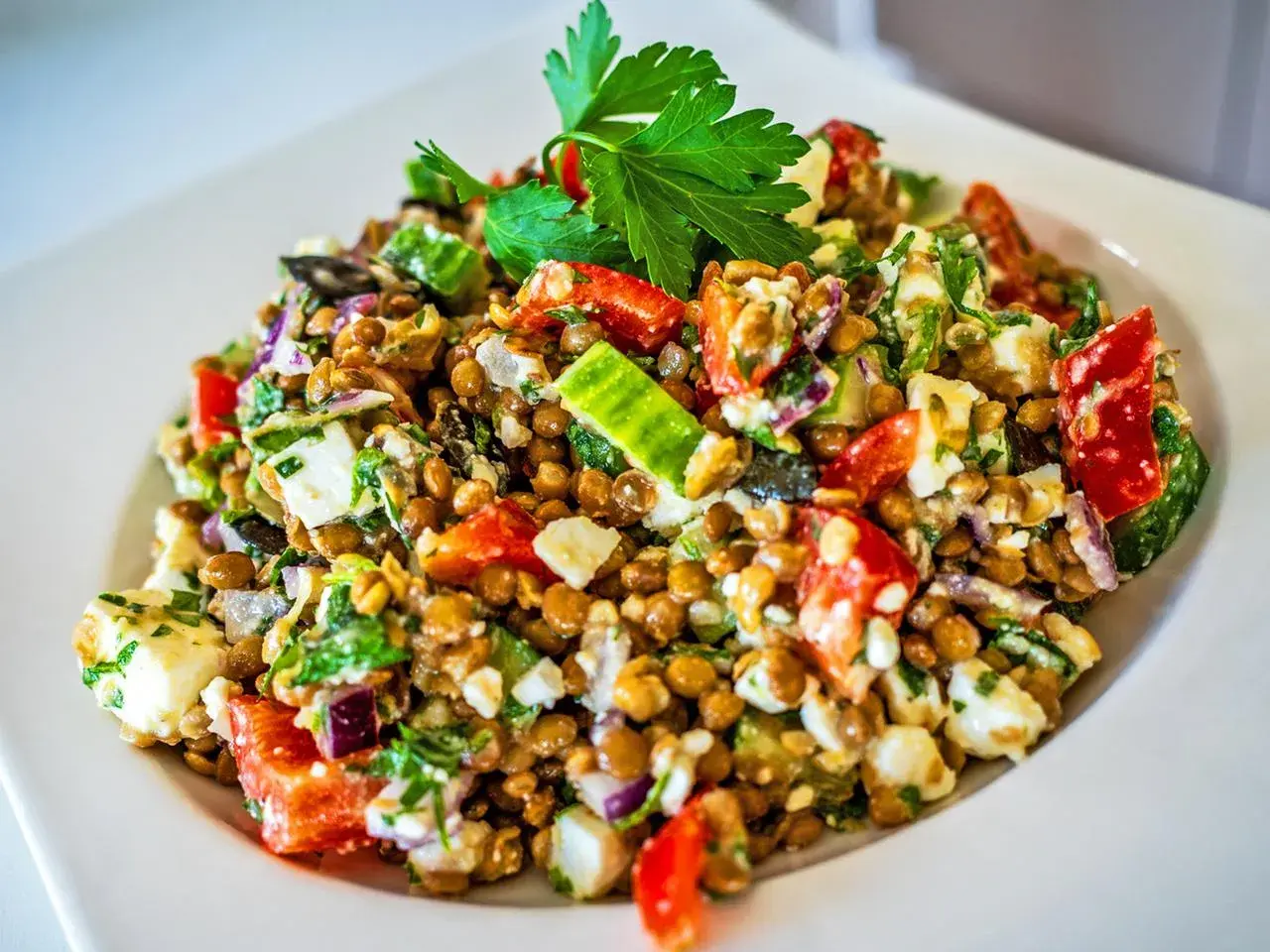 Ein bunter Linsensalat mit Feta, Gurken, Tomaten und roten Zwiebeln, garniert mit Petersilie.