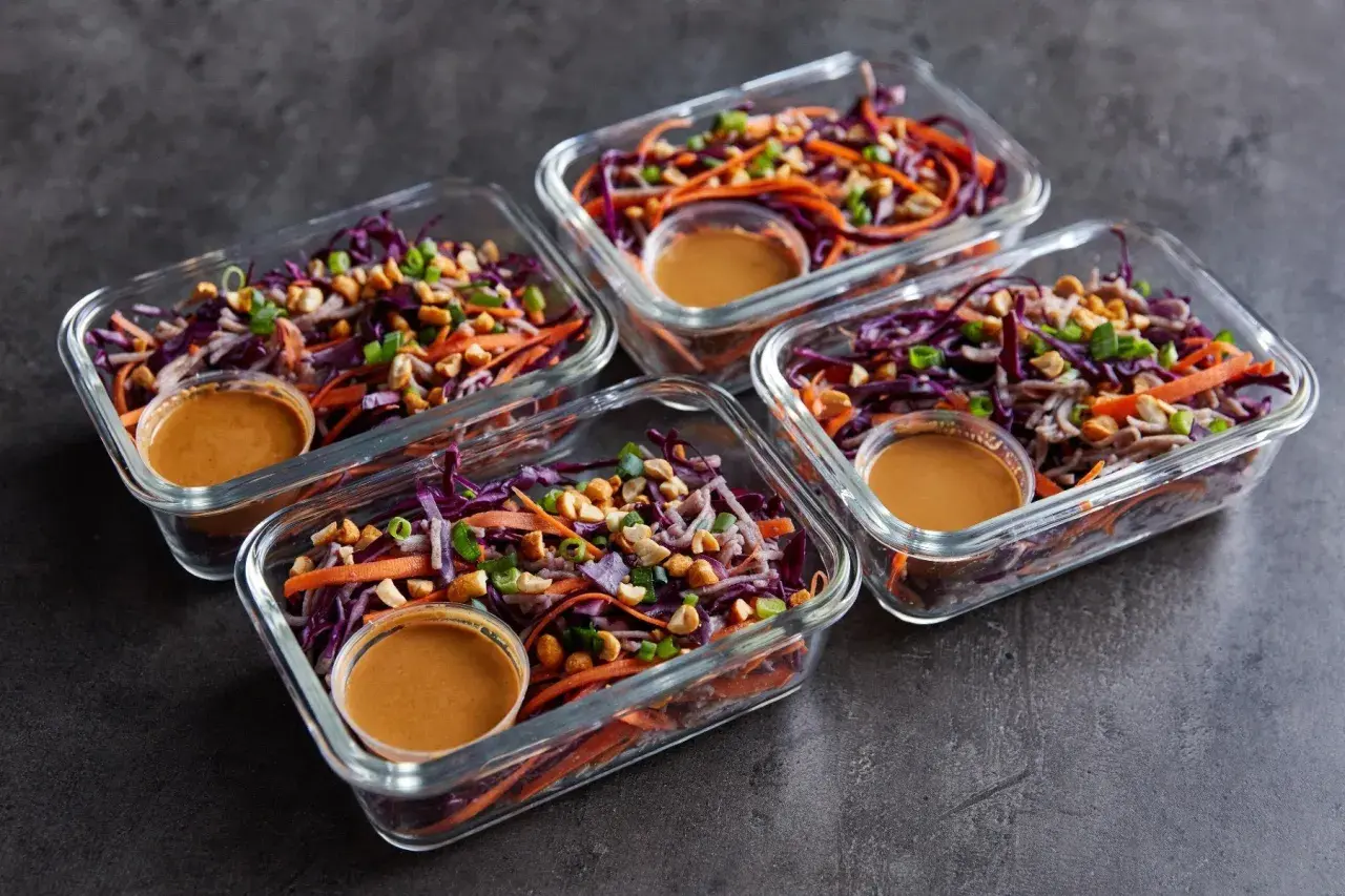 Vier Glasbehälter mit einem bunten Salat aus Rotkohl, Karotten und Erdnüssen. Perfekt für Rezepte mit viel Protein und wenig Kalorien.