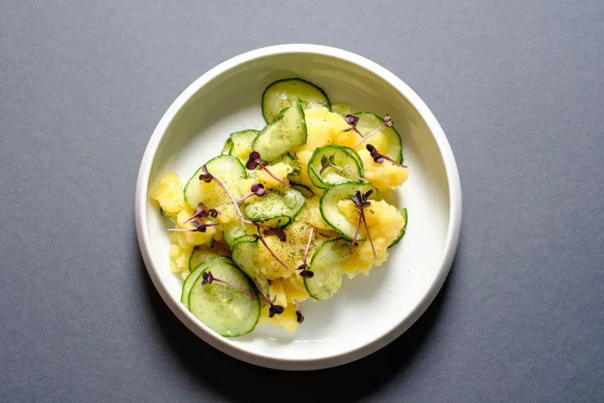 Ein köstlicher Kartoffelsalat mit frischen Gurkenscheiben, garniert mit zarten roten Sprossen und Dill.