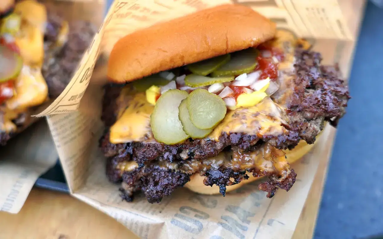 Saftige Burger-Patties mit geschmolzenem Käse, Gurken und Zwiebeln auf einem Brötchen, serviert auf Zeitungspapier.