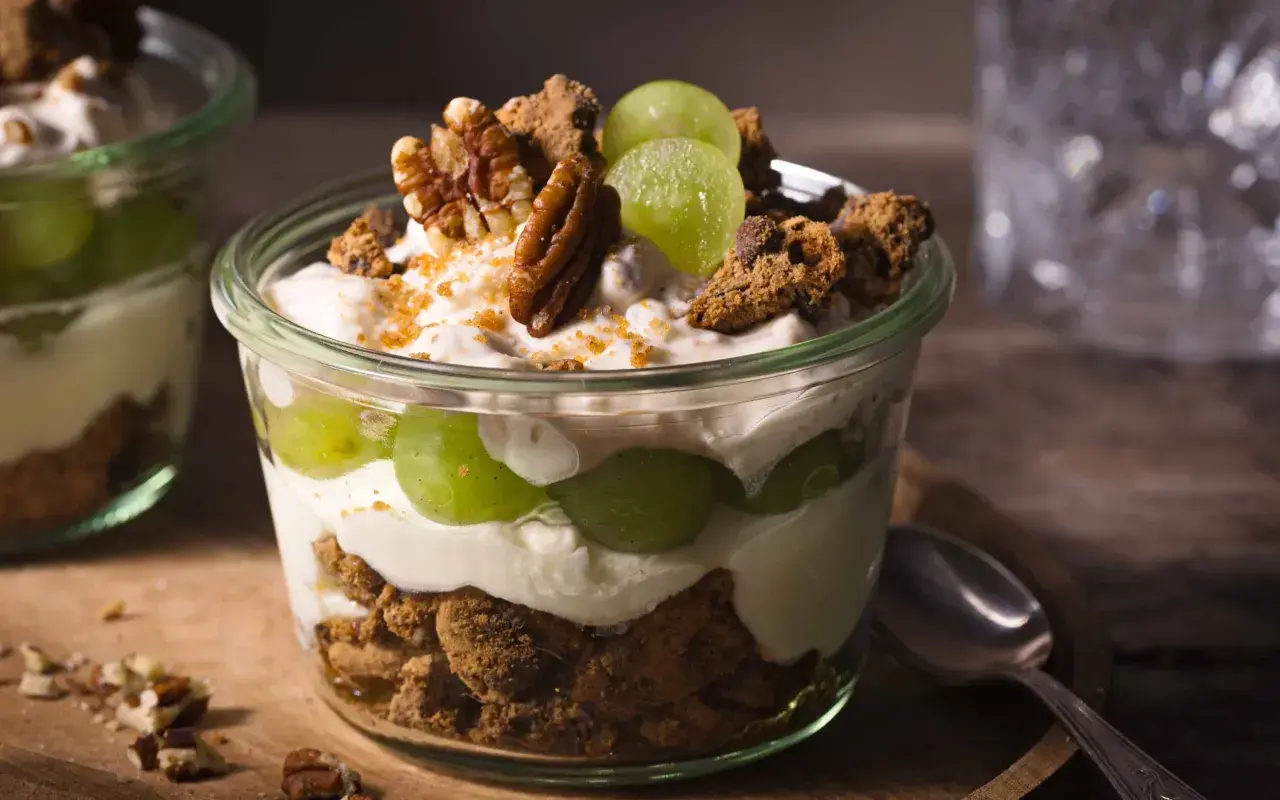 Ein köstliches Dessert im Glas: Schichten aus cremigem Joghurt, saftigen Weintrauben und knusprigen Cookie-Stücken, garniert mit Pekannüssen.
