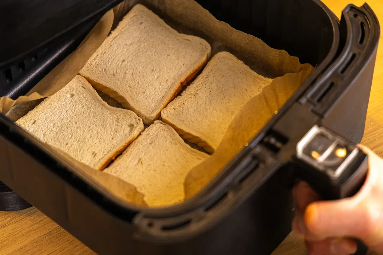 Vier Scheiben Toastbrot liegen in der Schublade eines Airfryers, bereit für ein schnelles Toast Hawaii.