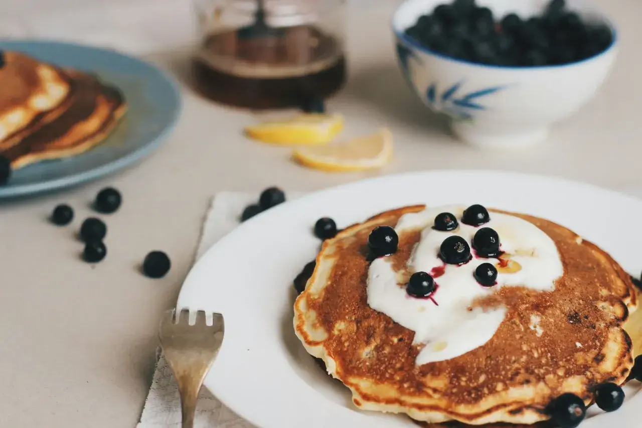 Leckere Pfannkuchen ohne Ei, garniert mit Joghurt und Blaubeeren, serviert mit Honig und Zitronenspalten.