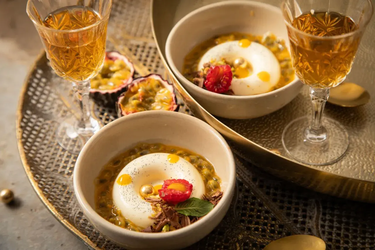 Zwei Panna Cotta-Desserts, inspiriert vom original italienischen Rezept, serviert mit Passionsfrucht und einem Hauch von Himbeere.