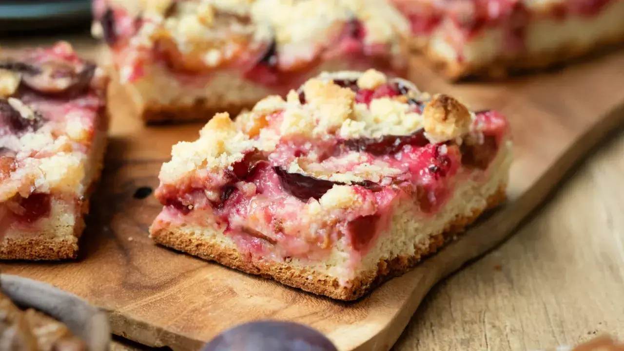 Saftiger Zwetschgenkuchen mit Streuseln auf einem Holzbrett. Ein Stück ist angeschnitten und zeigt die saftigen Früchte.