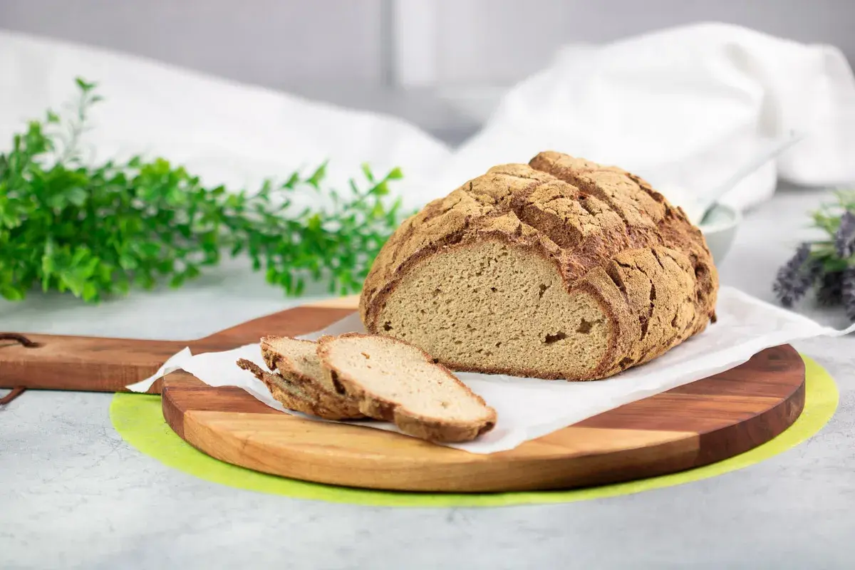 Ein rustikales Brot ohne Kohlenhydrate, aufgeschnitten auf einem Holzbrett, mit grünen Zweigen und Lavendel im Hintergrund.