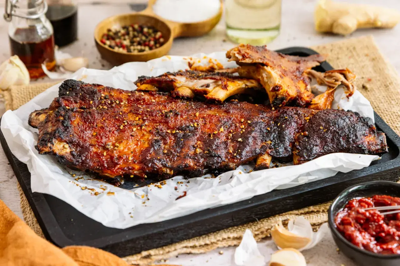 Saftige spareribs im backofen, glasiert und mit Gewürzen bestreut, serviert mit BBQ-Sauce.