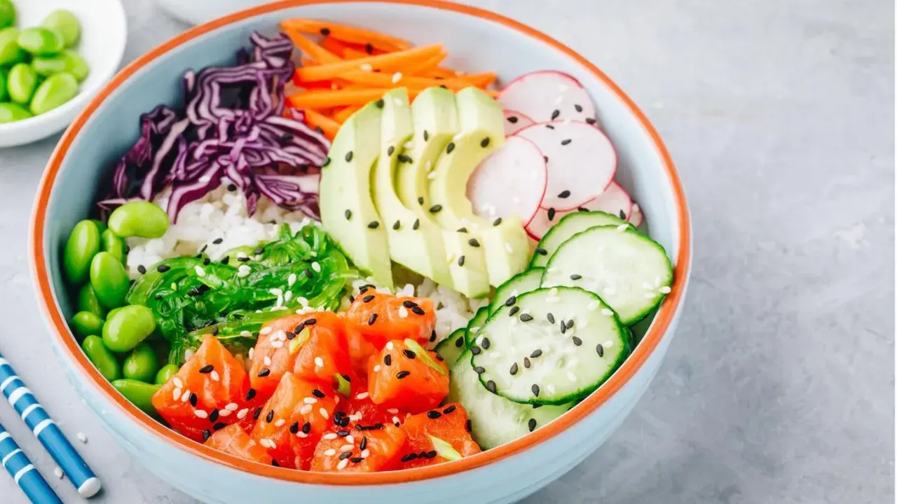 Bunte Poke Bowl mit Lachs, Avocado, Edamame, Gurke, Radieschen, Rotkohl und Seetang auf Reis.