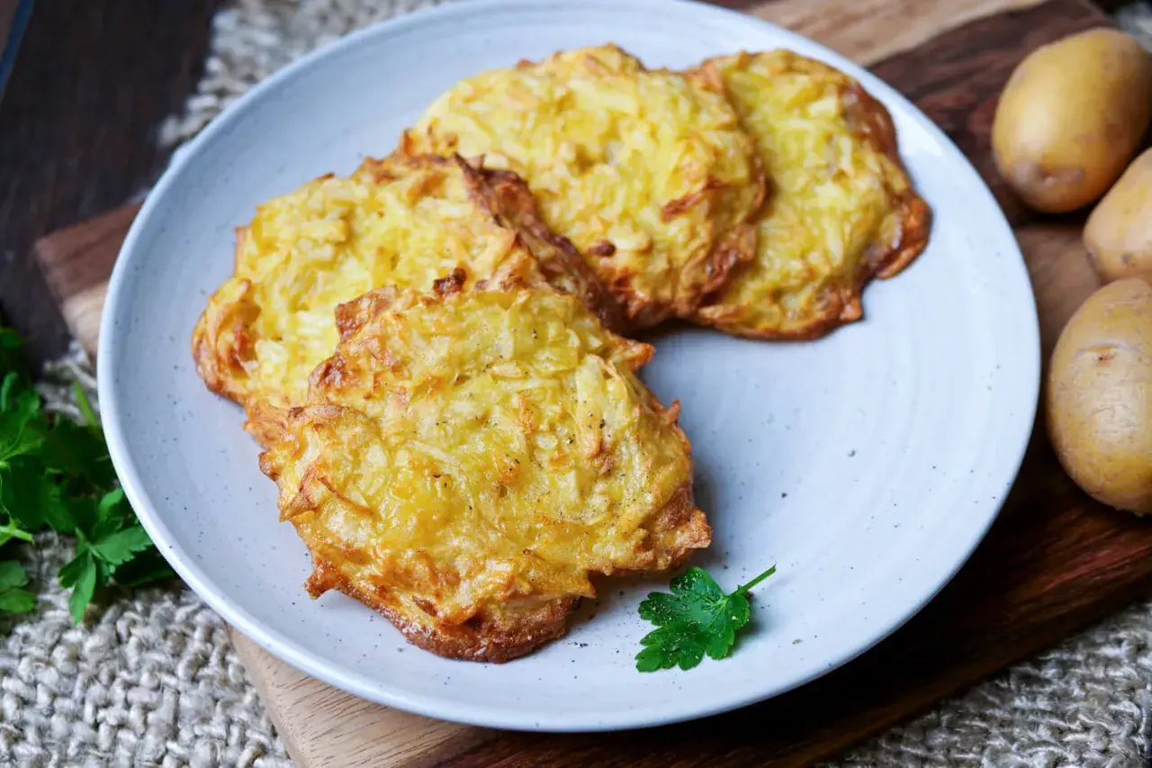 Goldbraune Kartoffelpuffer im Airfryer, knusprig und lecker, auf einem Teller mit Petersilie garniert.