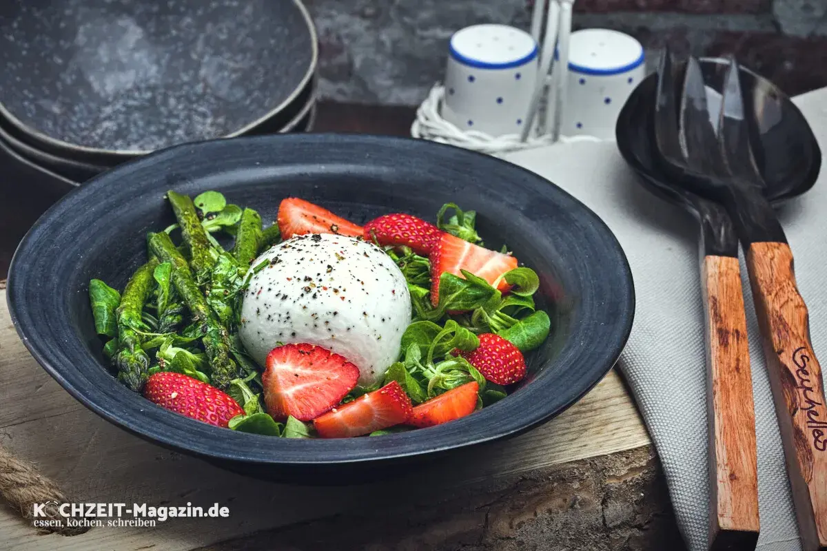 Ein frischer Spargelsalat mit Erdbeeren und Burrata, garniert mit Kräutern und Pfeffer.