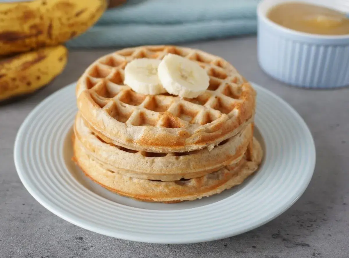 Stapel goldbrauner bananenwaffeln ohne zucker, garniert mit Bananenscheiben. Daneben liegen reife Bananen.