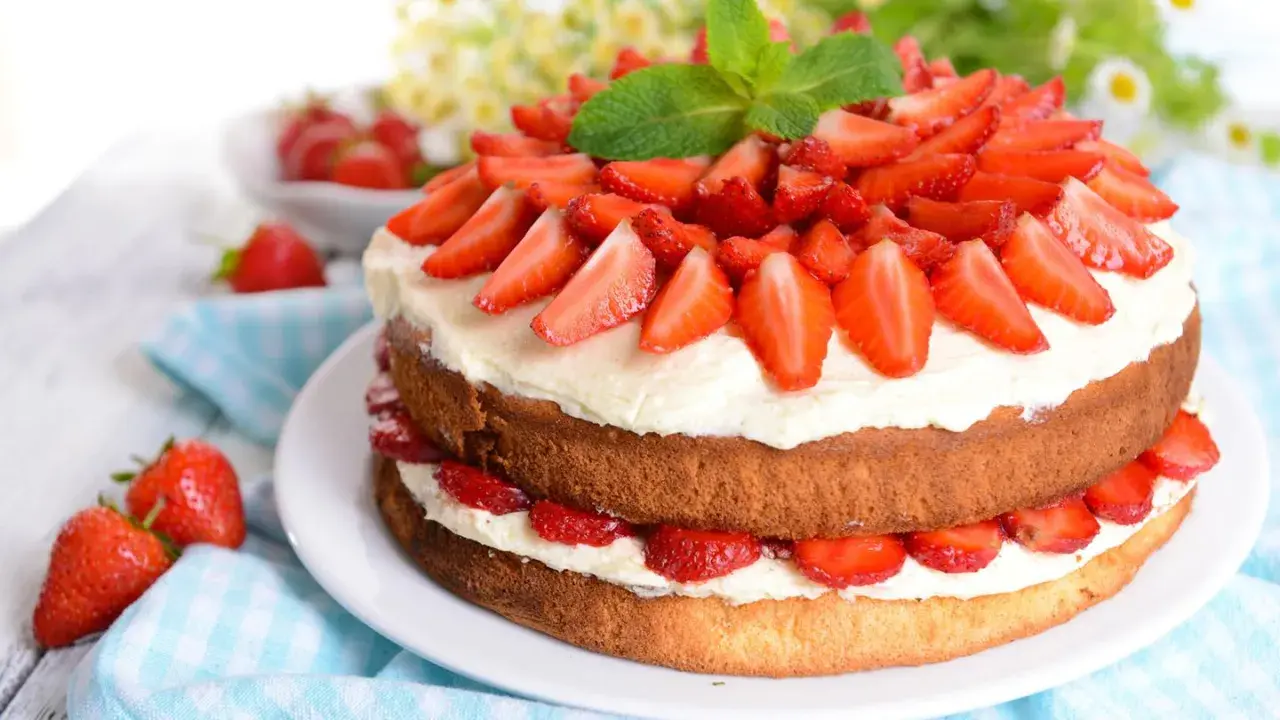 Eine zweistöckige Erdbeer-Sahne-Torte, üppig belegt mit frischen Erdbeerscheiben und garniert mit Minze.
