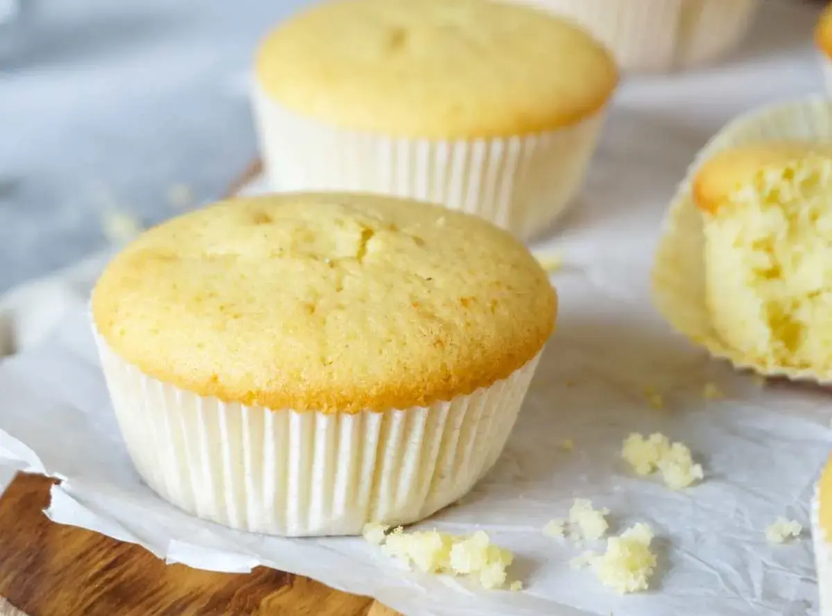 Frisch gebackene Vanille-Muffins, perfekt für ein einfaches Muffins Rezept. Einer ist angeschnitten und zeigt die saftige Krume.