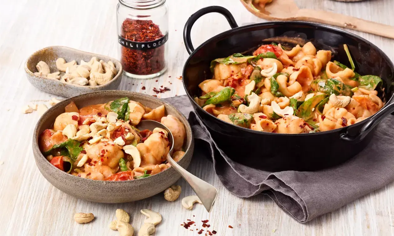 Ausgefallene Pasta-Rezepte vegetarisch: Cremige Muschelnudeln mit Cashews, Tomaten und Spinat, bestreut mit Chili-Flocken.