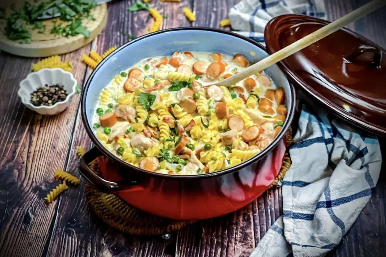 Herzhaftes Nudelgericht mit Würstchen, Erbsen und Hähnchen in cremiger Sauce. Köstliche gerichte mit sahne, garniert mit Petersilie.