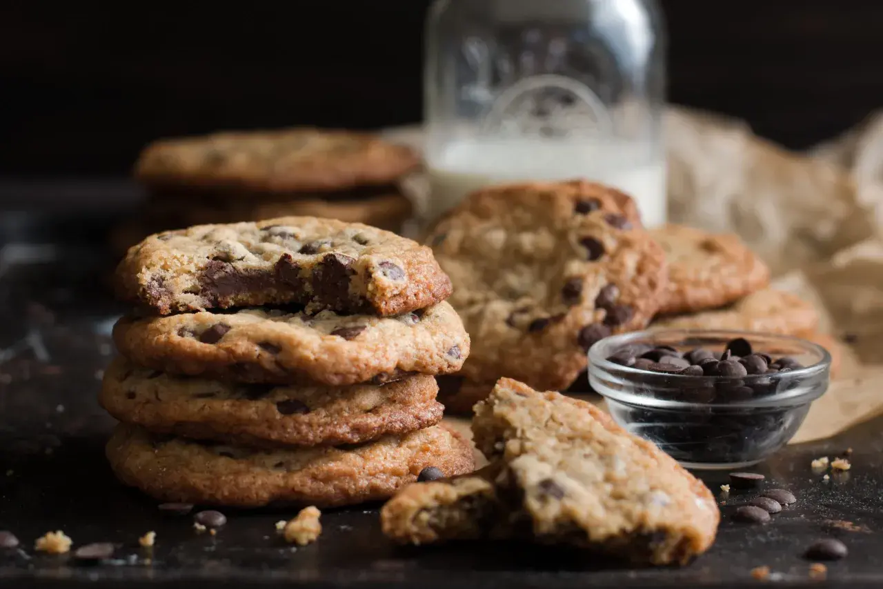 Ein Stapel saftiger Chocolate Chip Cookies, perfekt für ein einfaches Cookies Rezept. Daneben eine Schale Schokodrops und ein Glas Milch.