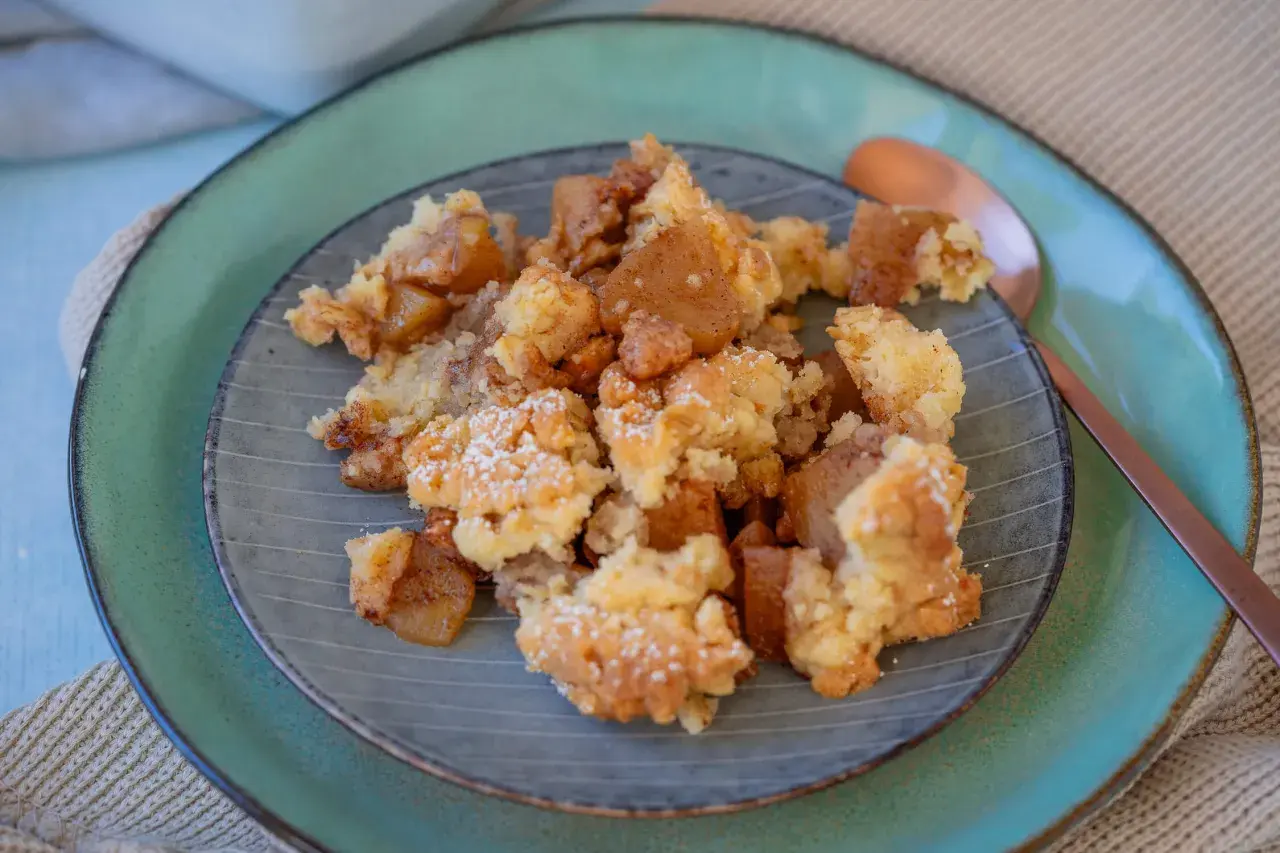 Ein Teller mit warmem Apfel Crumble, bestäubt mit Puderzucker. Die goldbraunen Apfelstücke und knusprigen Streusel laden zum Genießen ein.