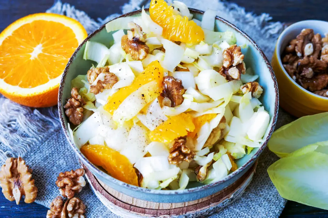 Erfrischender chicoree salat mit saftigen Orangenspalten und knackigen Walnüssen, garniert mit Pfeffer.