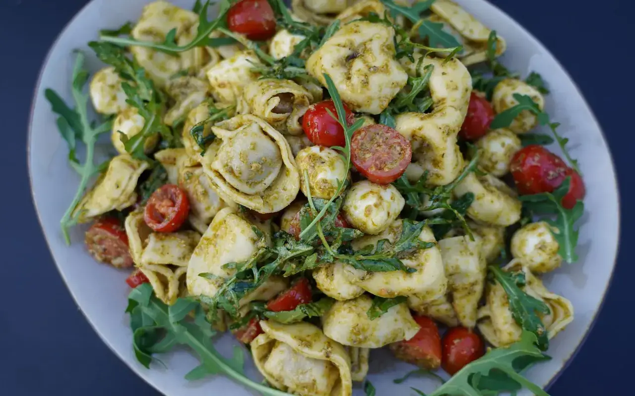 Mediterraner Salat mit Tortellini, Mozzarella-Bällchen, Kirschtomaten und Rucola, verfeinert mit Pesto.
