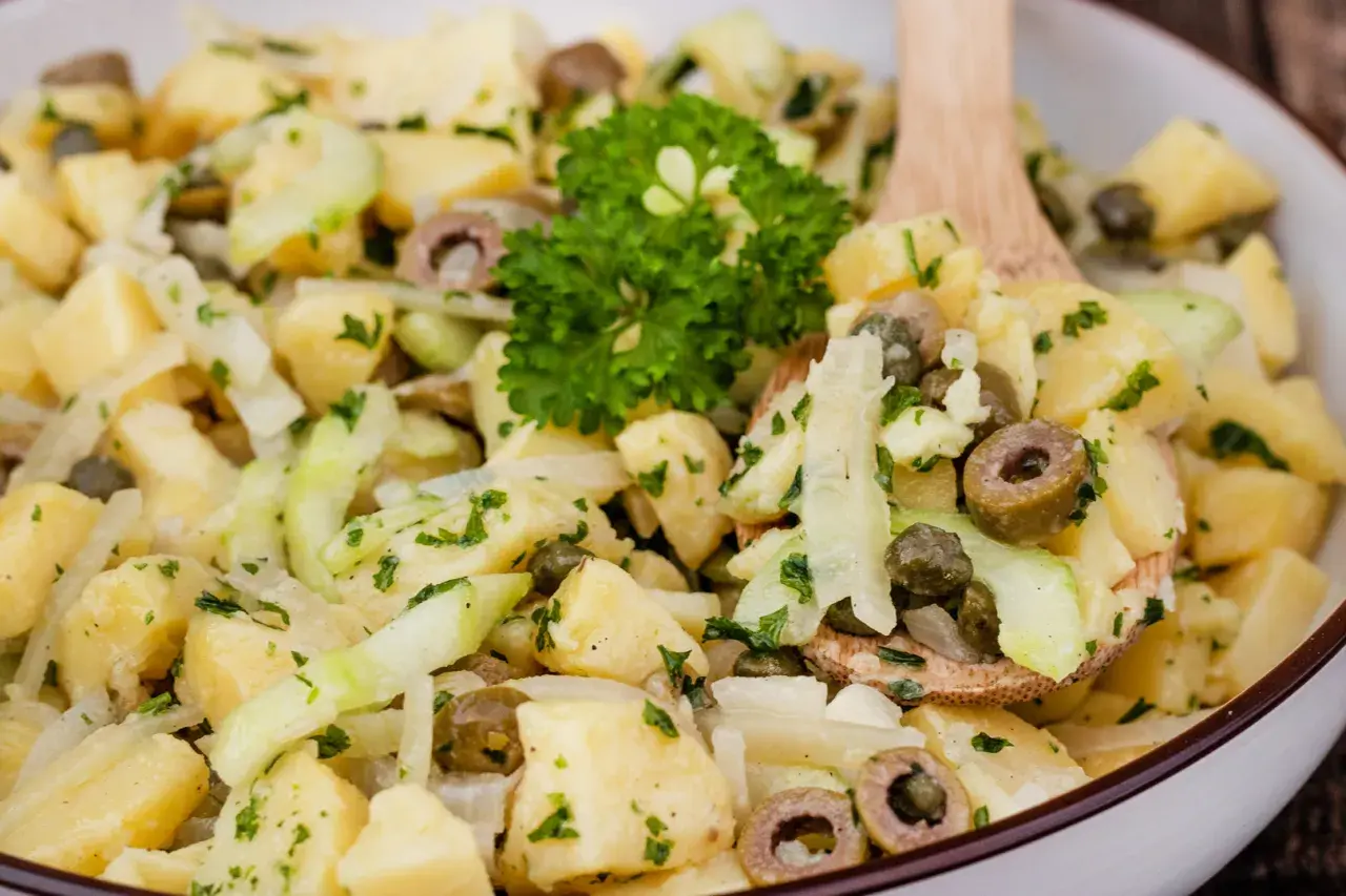 Ein köstlicher Kartoffelsalat ohne Mayo mit Gurken, Oliven und Kapern, garniert mit Petersilie.