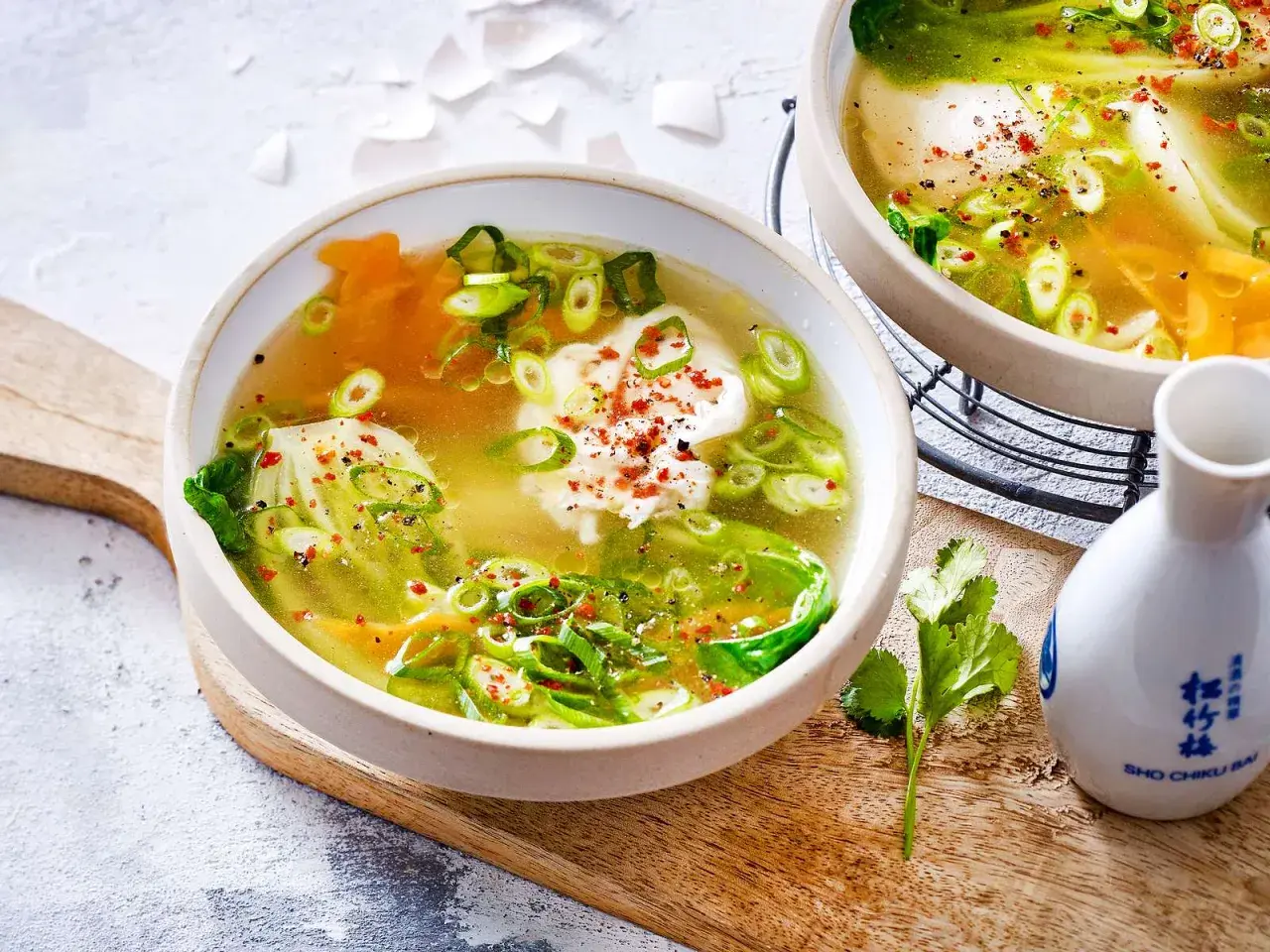 Zwei Schalen dampfender low carb suppe mit pochiertem Ei, Frühlingszwiebeln und Pak Choi, garniert mit Chiliflocken.