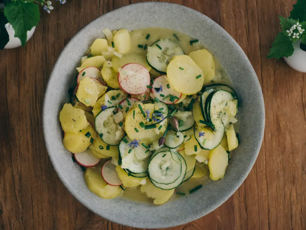 Bayrischer Kartoffelsalat mit Speck und Zwiebeln, garniert mit Radieschen, Gurken und Schnittlauch. Ein deftiger Genuss!
