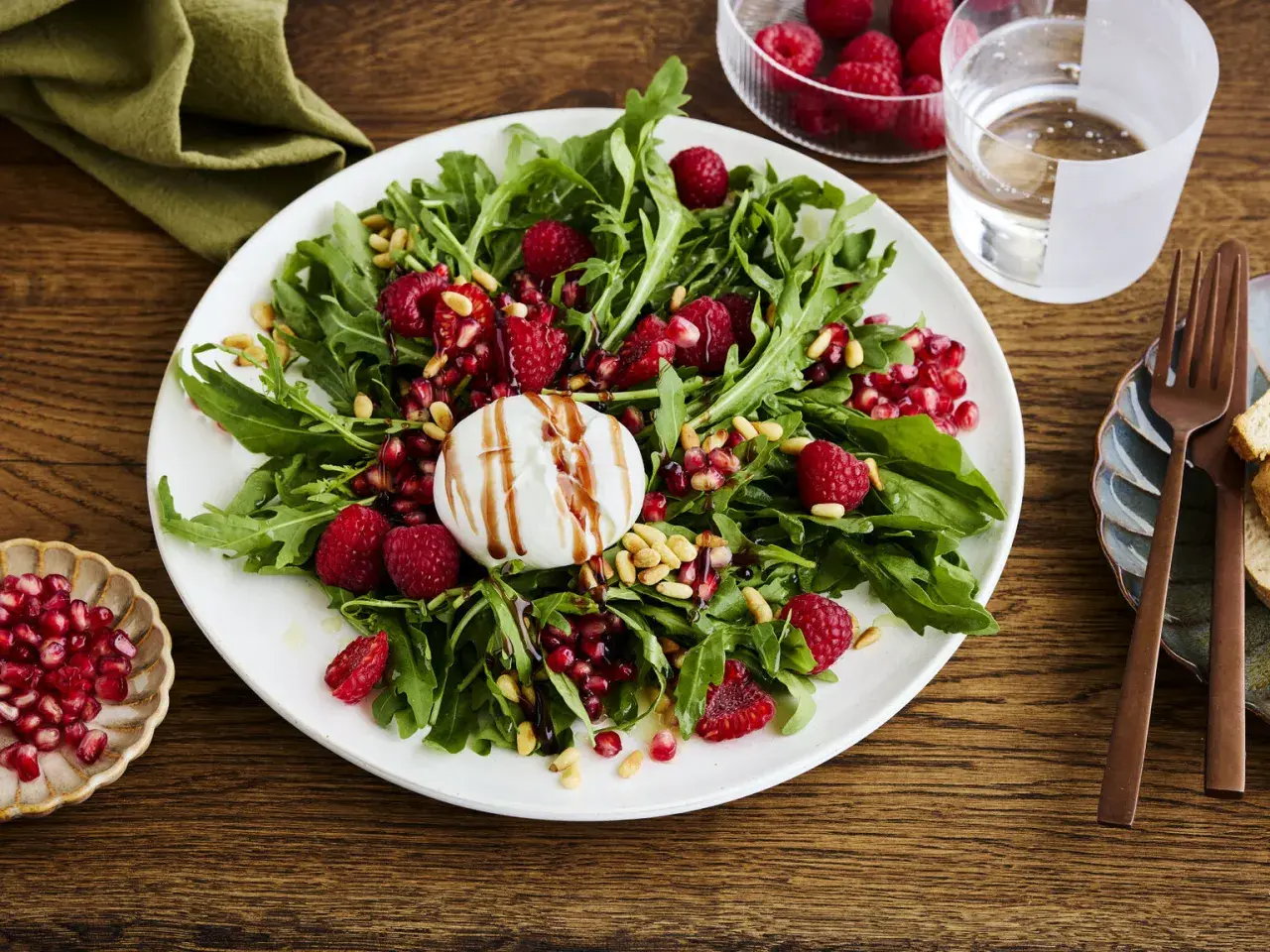Ein frischer Salat mit Rucola, Himbeeren, Granatapfelkernen und Pinienkernen, gekrönt von cremiger Burrata. Perfekt für leichte Burrata Rezepte.