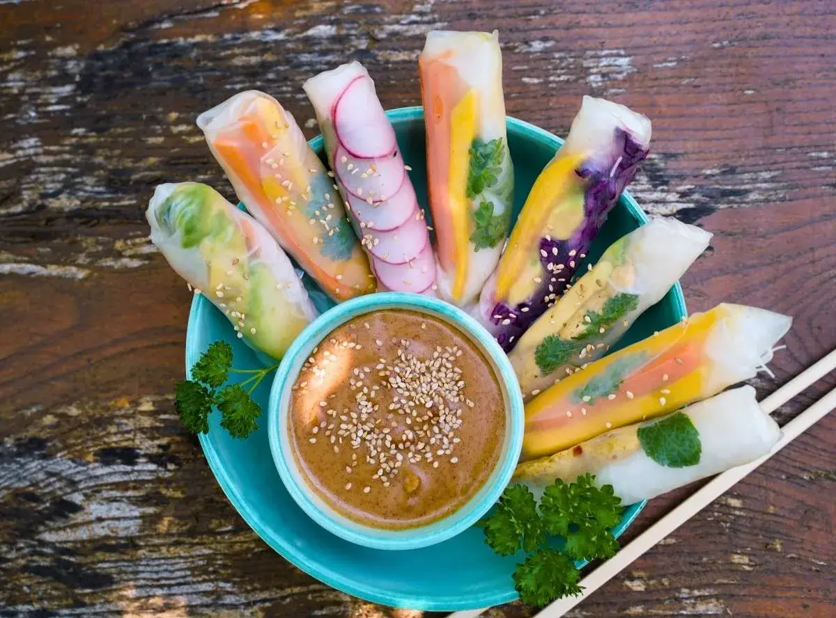 Frische Sommerrollen mit bunten Gemüsesorten, garniert mit Sesam, serviert mit Erdnussdip. Perfekt für ein leichtes Sommerrollen Rezept.