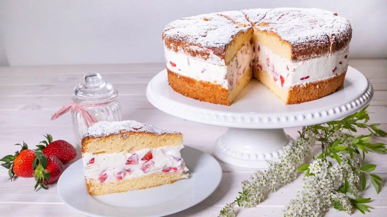 Eine köstliche Erdbeer Sahne Torte, mit frischen Erdbeeren und Puderzucker bestäubt, wartet darauf, genossen zu werden. Ein Stück ist bereits auf einem Teller angerichtet.
