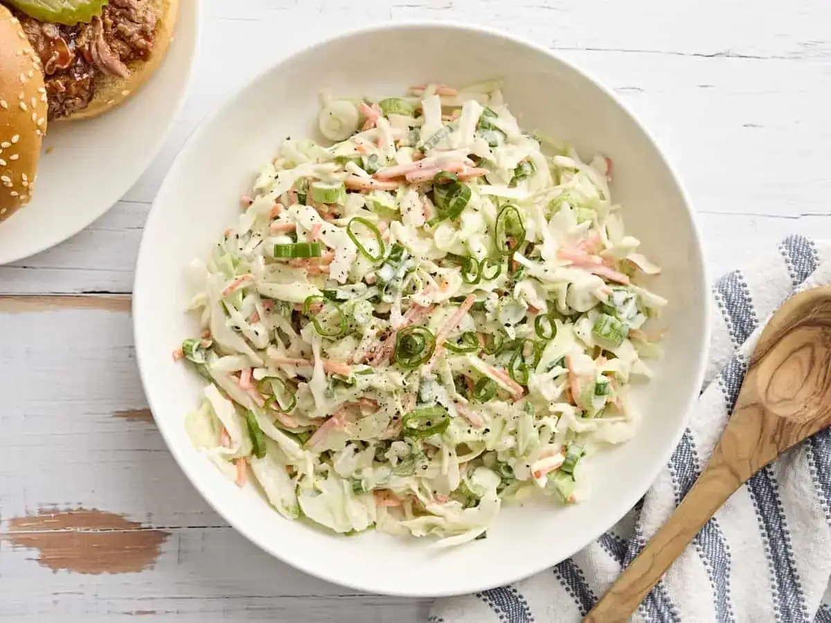 Cremiger Krautsalat mit Karotten und Frühlingszwiebeln, perfekt für Ihr coleslaw rezept. Daneben ein Burger mit Pulled Pork.