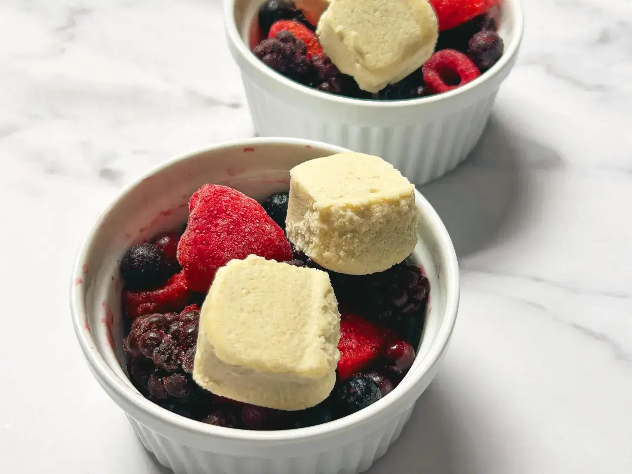 Zwei weiße Schalen gefüllt mit Beeren und Teigstücken. Perfekt für einfache und schnelle Torten Rezepte.