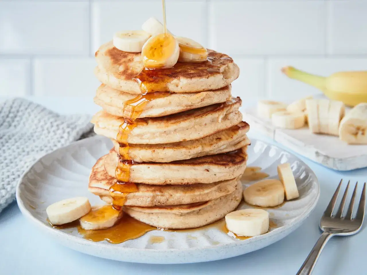 Ein Stapel fluffiger Bananen-Pancakes, betr&auml;ufelt mit Sirup und garniert mit Bananenscheiben.