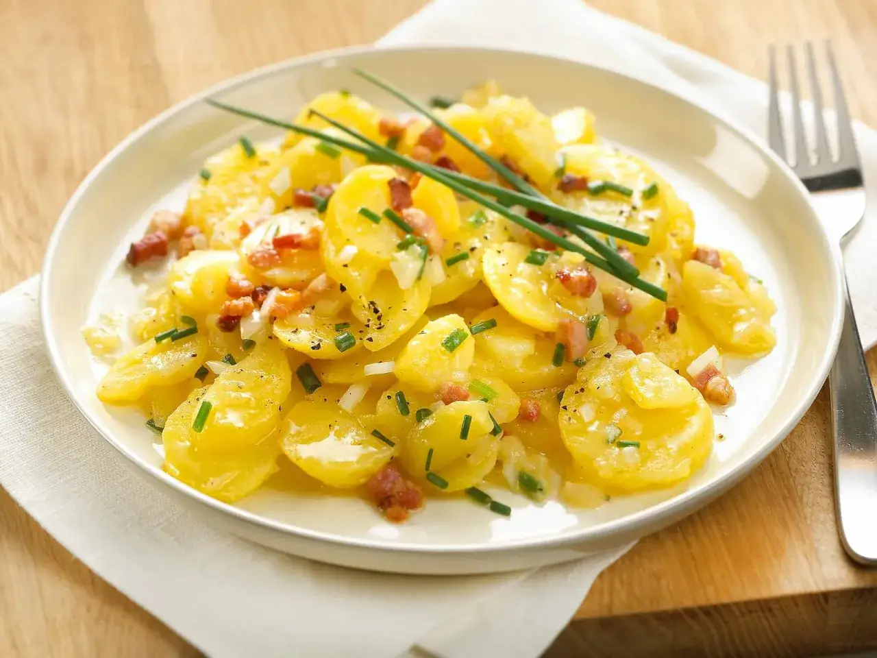 Ein Teller mit bayrischem Kartoffelsalat mit Speck und Zwiebeln, garniert mit Schnittlauch.