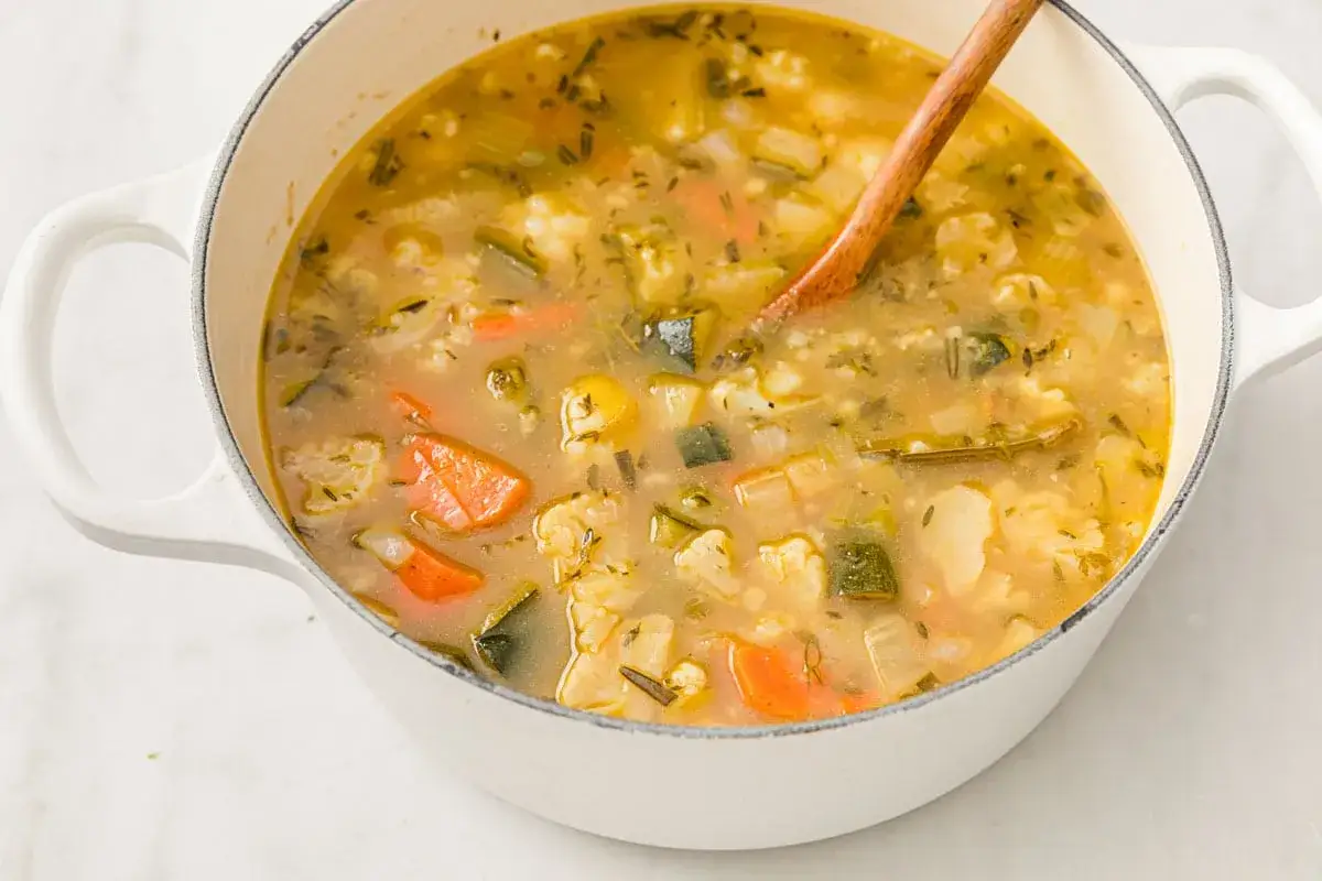Herzhafte low carb suppe mit viel Gemüse wie Karotten, Zucchini und Blumenkohl in einem weißen Topf, bereit zum Servieren.