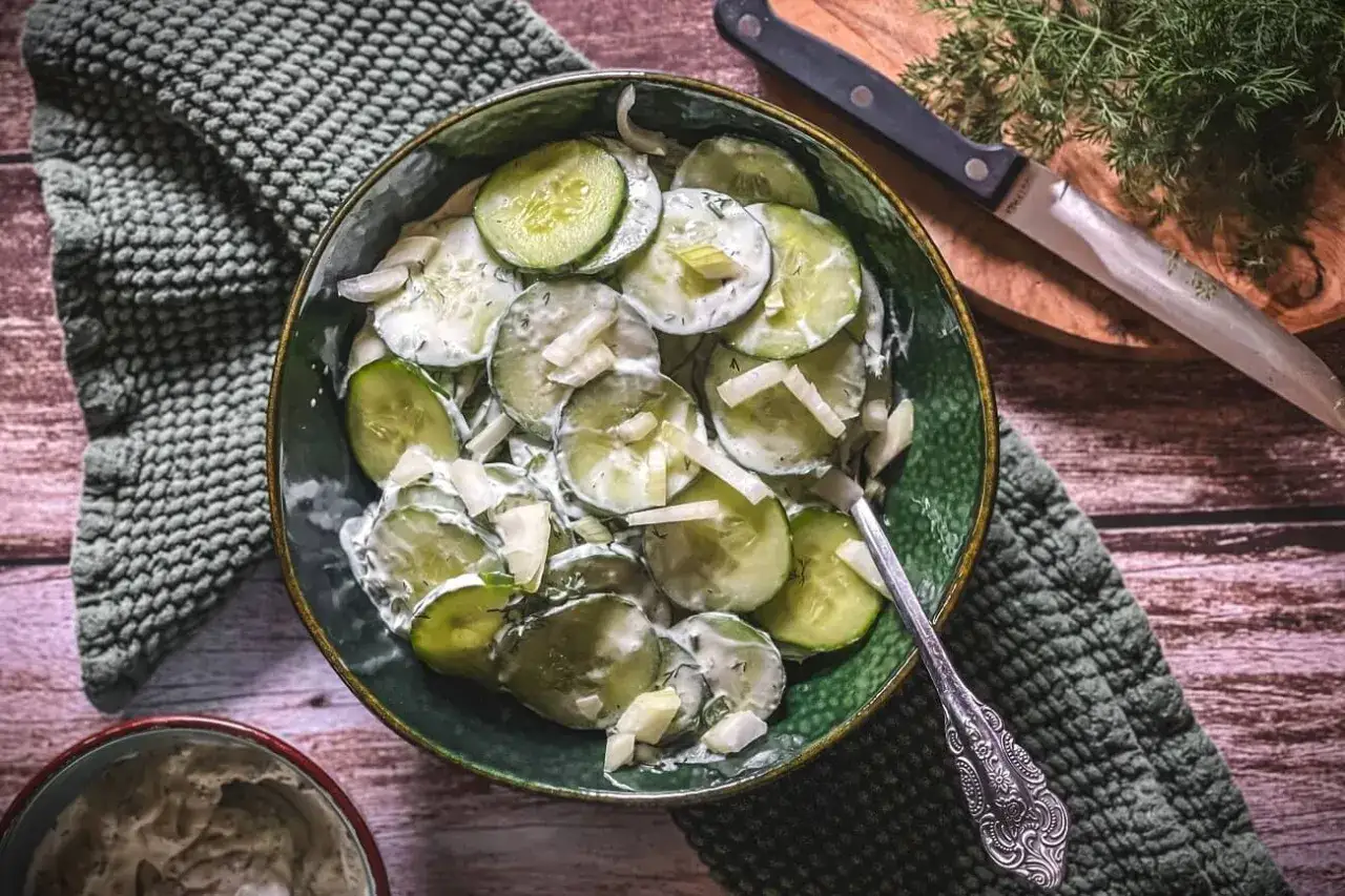 Frischer gurkensalat mit schmand und Dill, garniert mit Zwiebeln, serviert in einer grünen Schüssel.