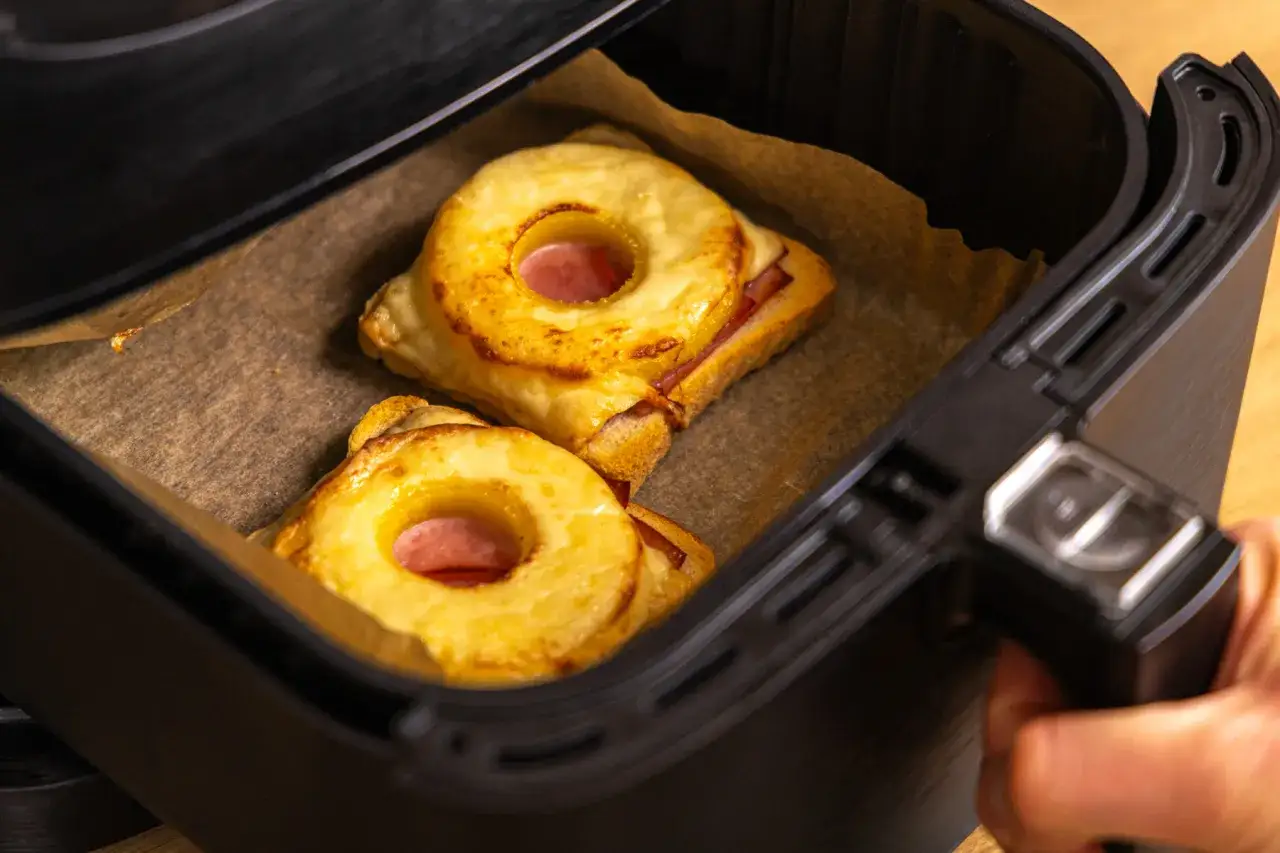 Zwei goldbraune Toast Hawaii mit Ananasringen und Schinken in der Airfryer-Schublade, bereit zum Genie&szlig;en.