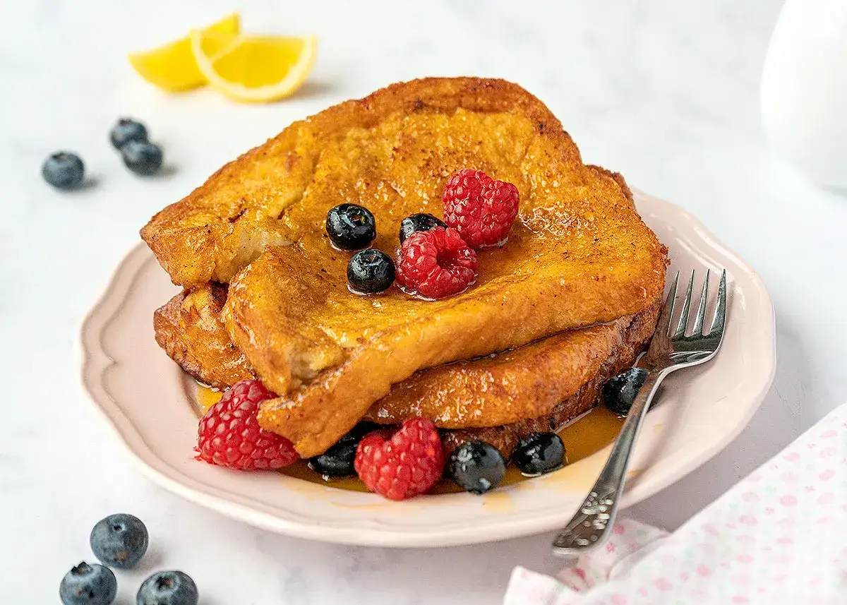 Goldbrauner French Toast mit Beeren und Zitronenspalten auf einem rosa Teller. Ein perfekter Start in den Tag!